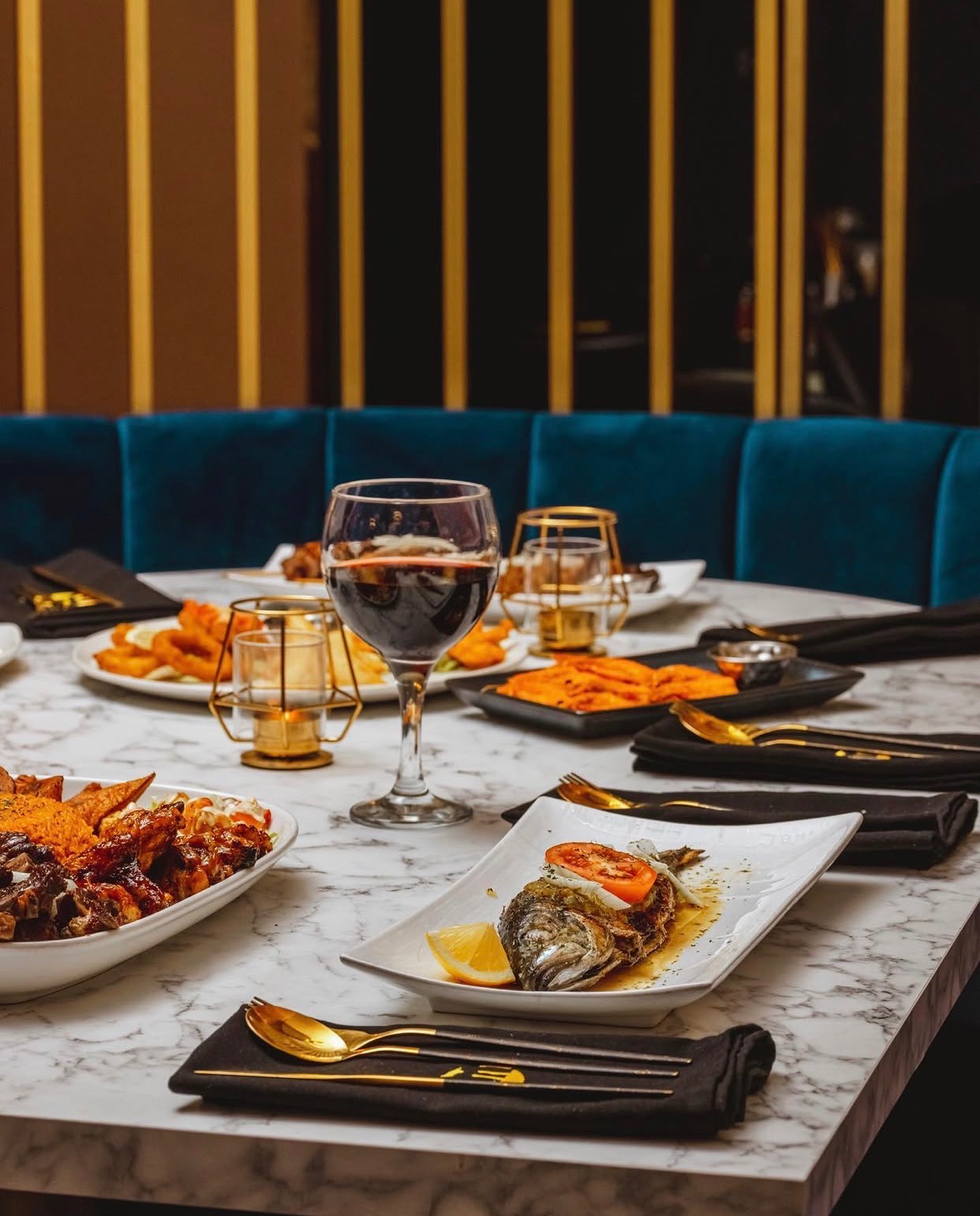 Congolese dishes, wine and gold cutlery on a marble table beside blue velvet seating at Deluxe Manna