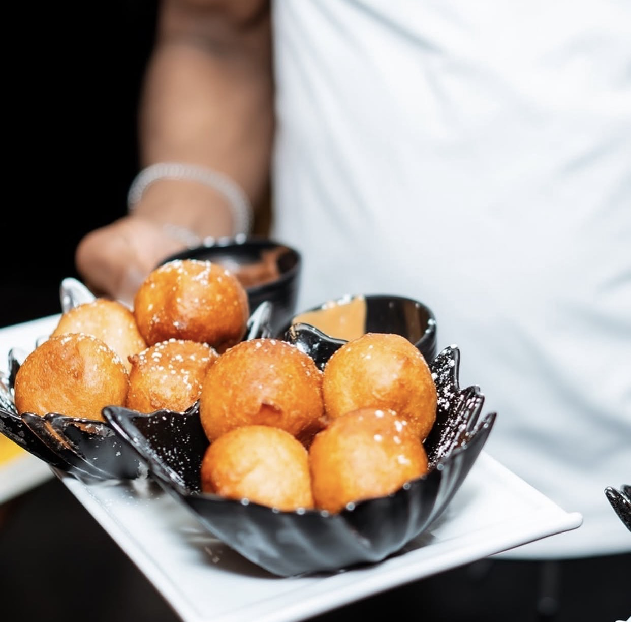Golden puff puffs served warm in a sculpted black bowl with dips